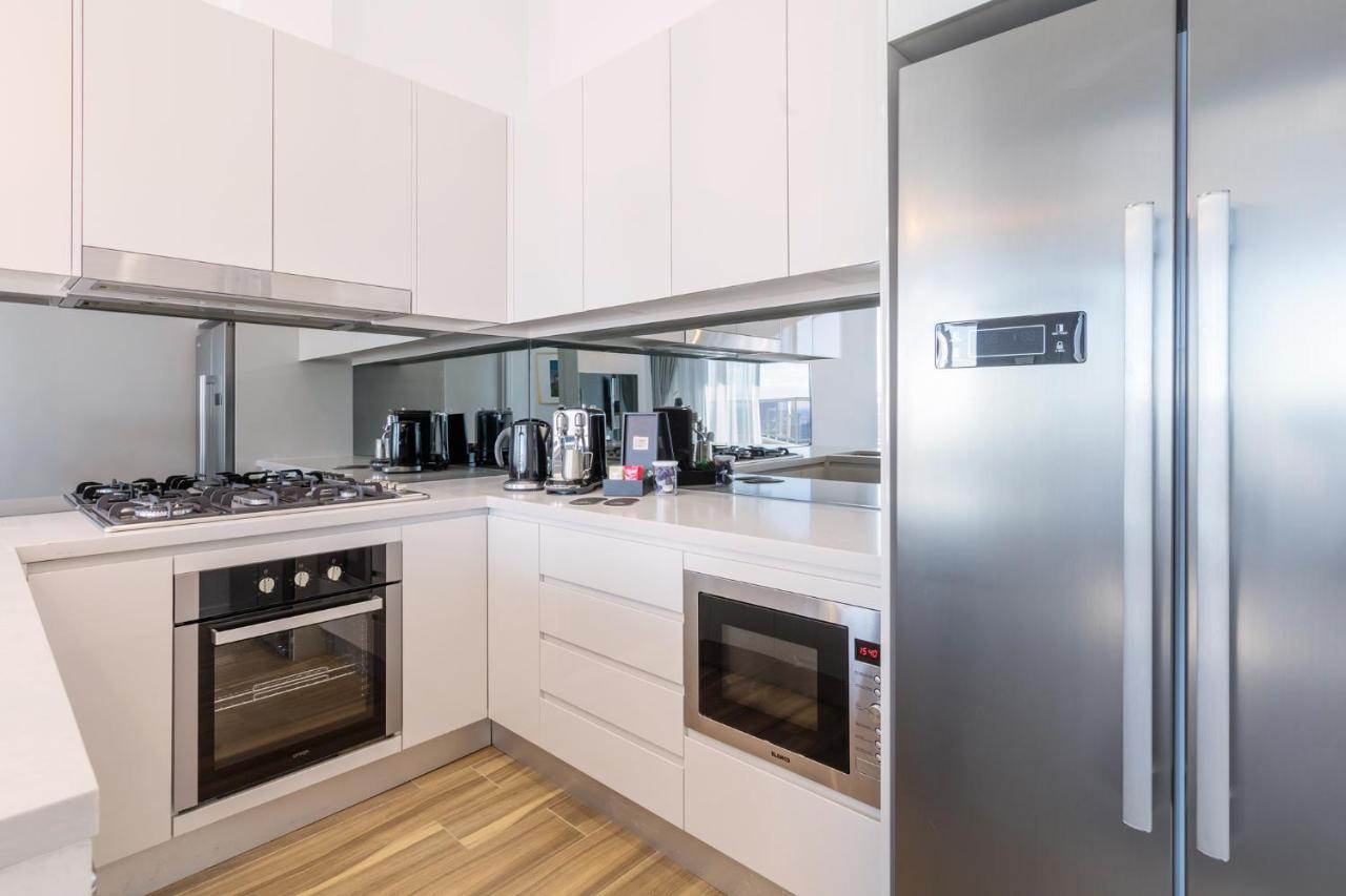 Meriton Suites Bondi Junction Sídney Exterior foto The photo shows a modern kitchen with a clean and minimalist design. It features white cabinetry and a stainless steel refrigerator. The kitchen includes a gas stove with an oven below it, as well as a microwave. There are several kitchen appliances,