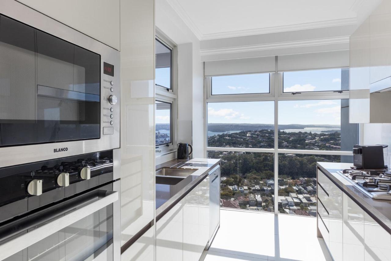 Meriton Suites Bondi Junction Sídney Exterior foto The photo shows a modern kitchen with sleek, shiny white cabinets and a large window that offers a panoramic view of the outside landscape. The kitchen features built-in appliances, including an oven and a stove, with a stylish countertop. The spacio