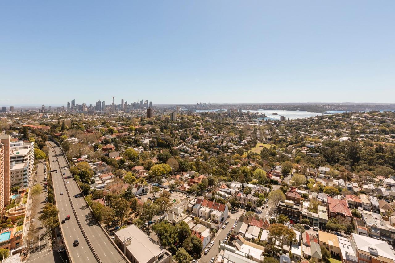 Meriton Suites Bondi Junction Sídney Exterior foto The photo captures a panoramic view of a vibrant urban landscape. In the foreground, there are residential areas with various houses and greenery, showcasing a suburban environment. In the background, the skyline of a city can be seen, featuring tall