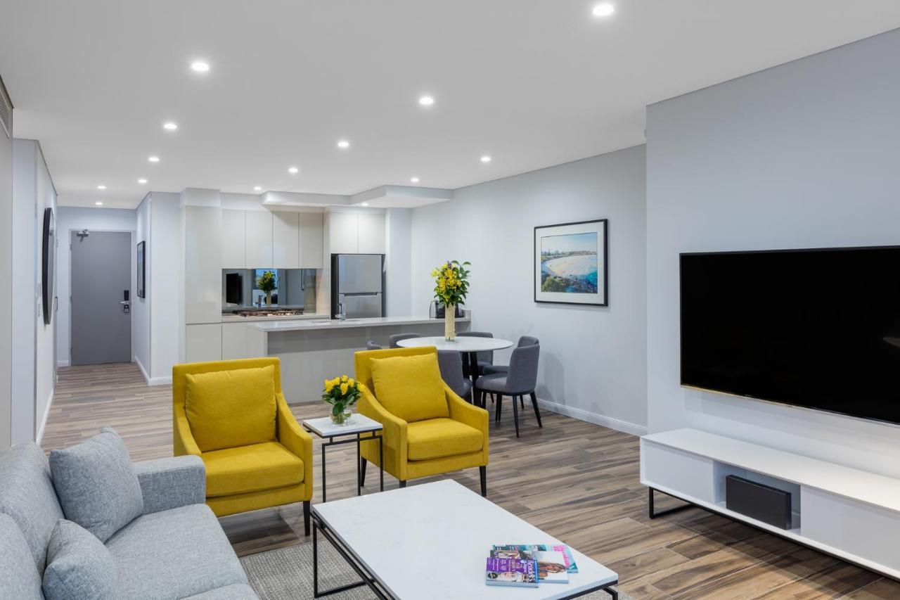 Meriton Suites Bondi Junction Sídney Exterior foto The photo shows a modern living space that includes a cozy sitting area and a dining area. The sitting area features two bright yellow chairs and a light gray sofa, arranged around a coffee table. There are decorative items on the table, including fl