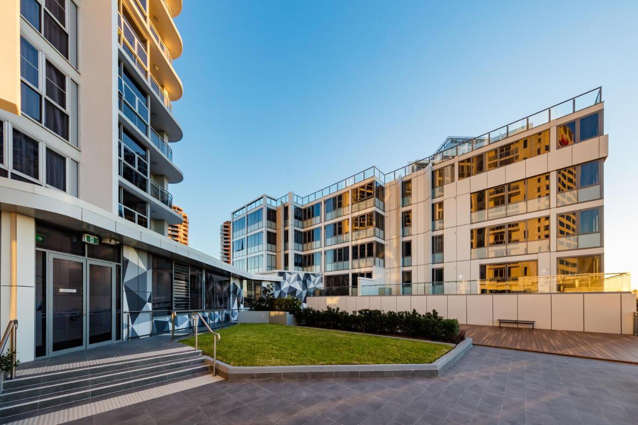 Meriton Suites Bondi Junction Sídney Exterior foto The photo showcases a modern residential area featuring contemporary buildings. In the foreground, there is a landscaped green space surrounded by well-designed architecture. The buildings have large glass windows, reflecting the light, and feature a