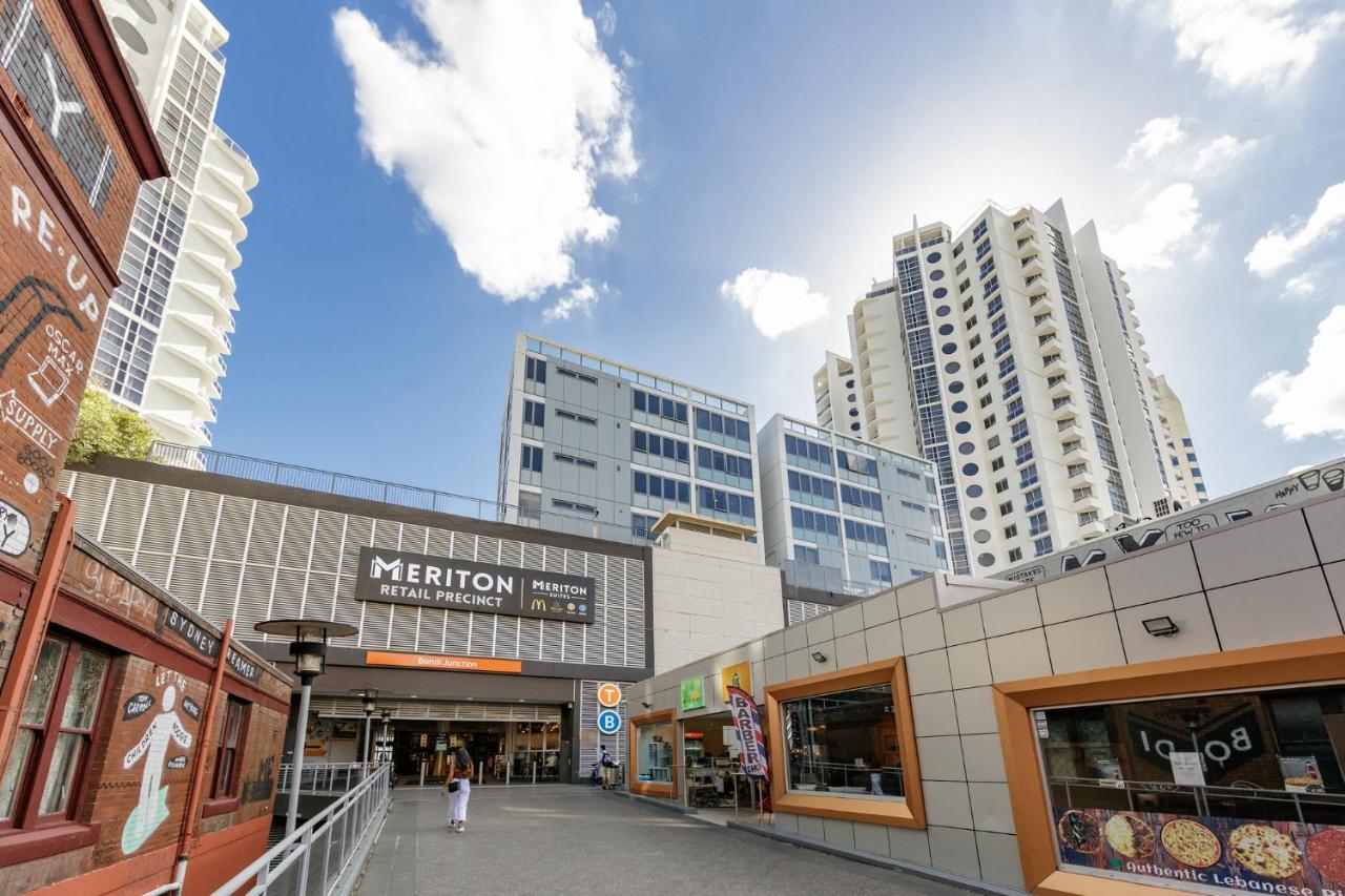 Meriton Suites Bondi Junction Sídney Exterior foto The photo depicts a modern urban environment featuring a building labeled "Meriton Retail Precinct." In the foreground, there are shops with colorful signage, while in the background, tall residential buildings tower over the area. The sky above is b