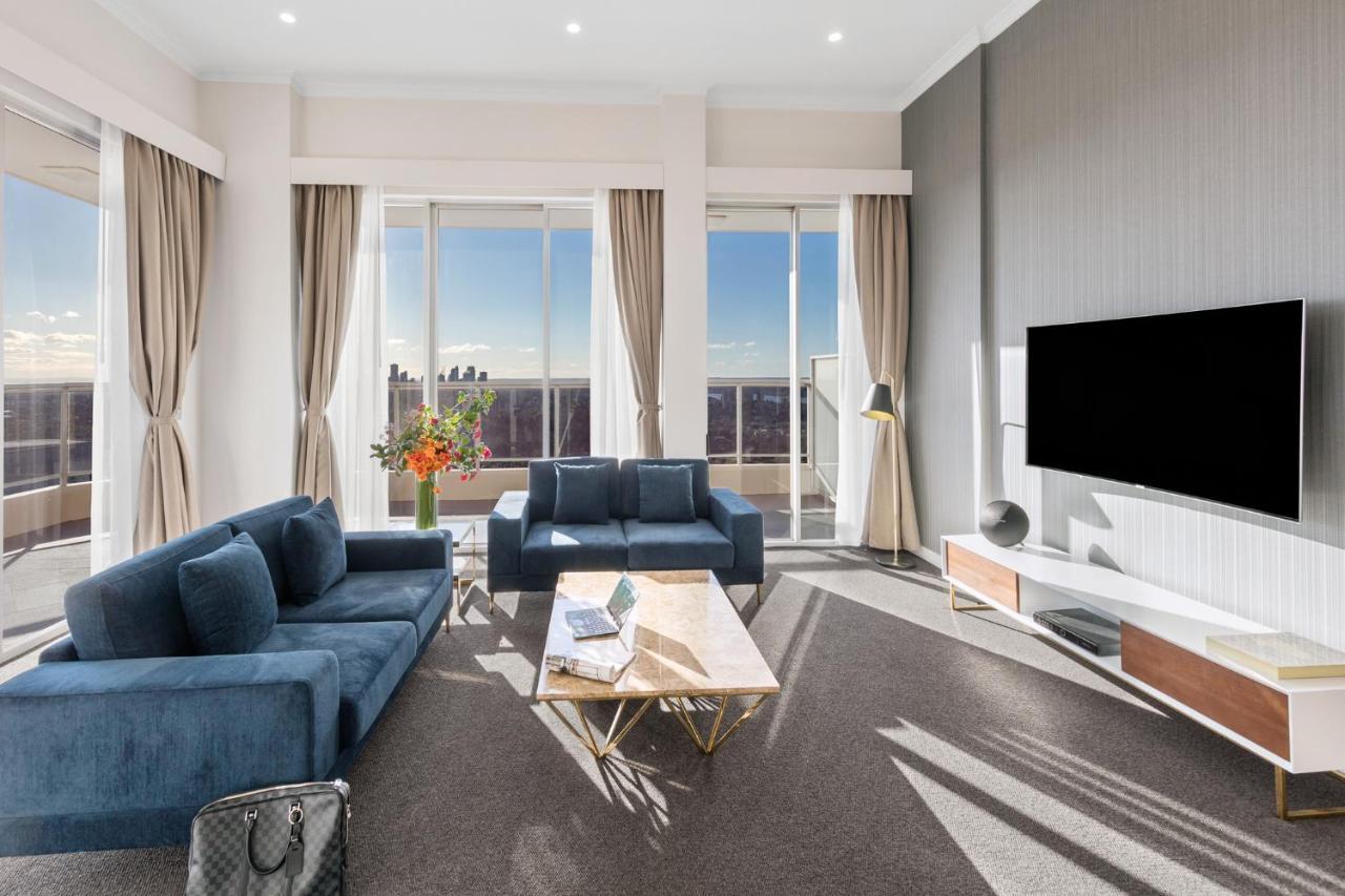 Meriton Suites Bondi Junction Sídney Exterior foto The photo depicts a modern living room with a stylish and contemporary design. It features a cozy seating arrangement with a blue sofa and two matching armchairs. In front of the seating area is a coffee table with a geometric design. The room has la