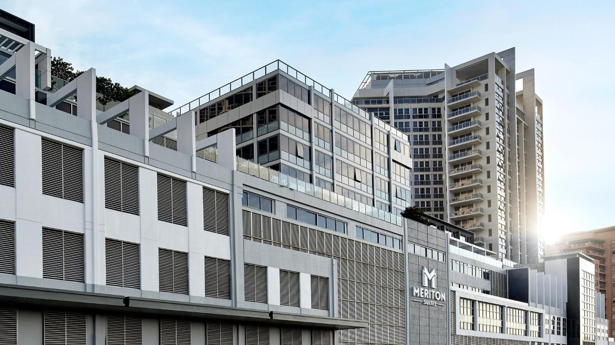 Meriton Suites Bondi Junction Sídney Exterior foto The image shows a modern urban building or complex. The structure features a combination of glass and concrete elements, showcasing contemporary architectural design. The foreground has a lower section that appears to be a podium or base with a textu
