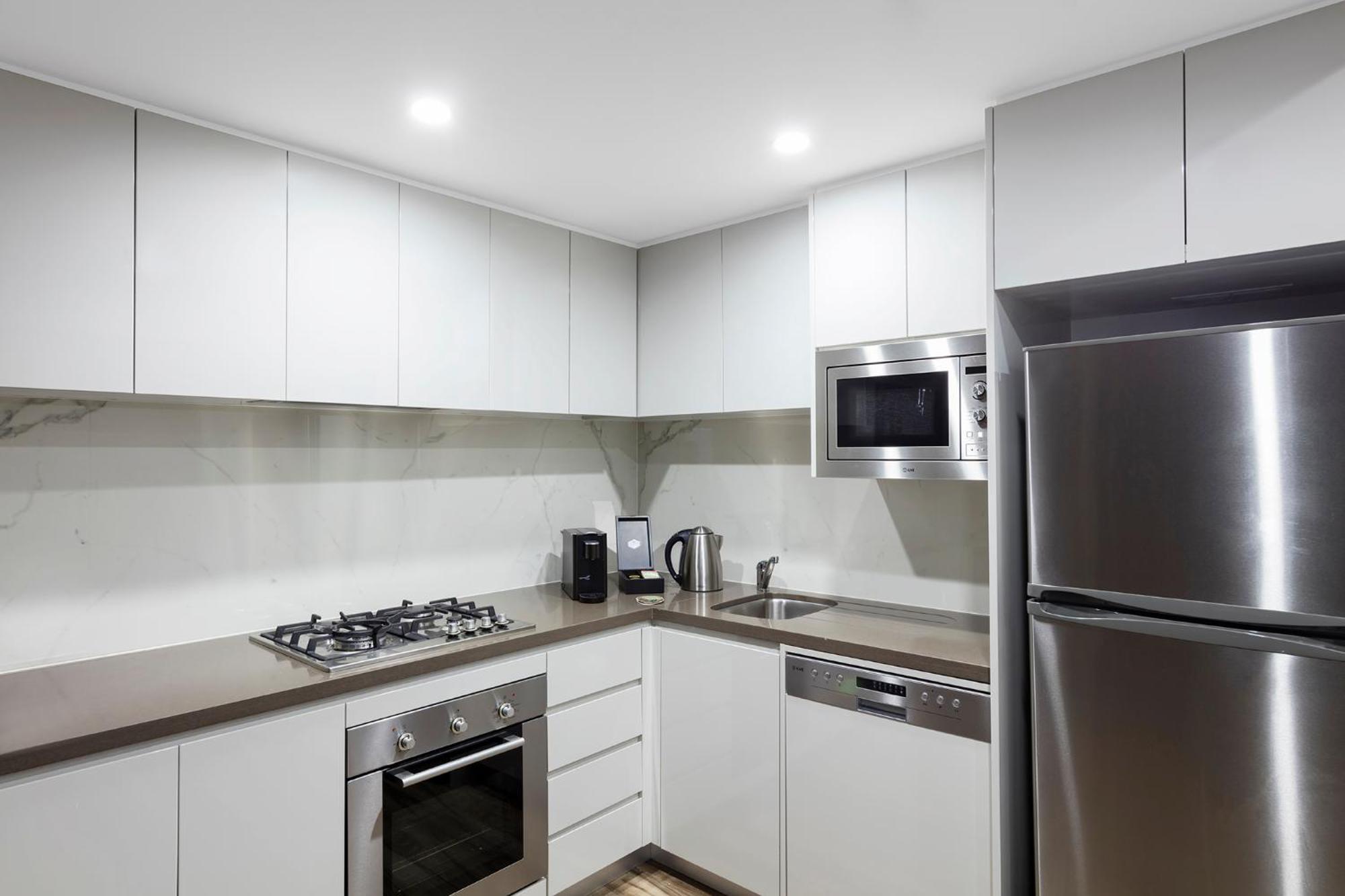 Meriton Suites Bondi Junction Sídney Exterior foto The photo shows a modern kitchen featuring a minimalist design. It has light-colored cabinetry, a countertop, and stainless steel appliances. The appliances include a gas stove with multiple burners, an oven, a microwave, a kettle, and a refrigerator